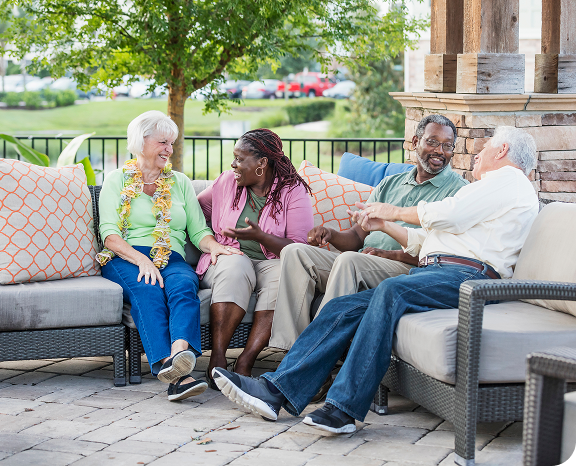 A group of elderly people sitting comfortably on couches in a cozy patio area, enjoying each other's company.